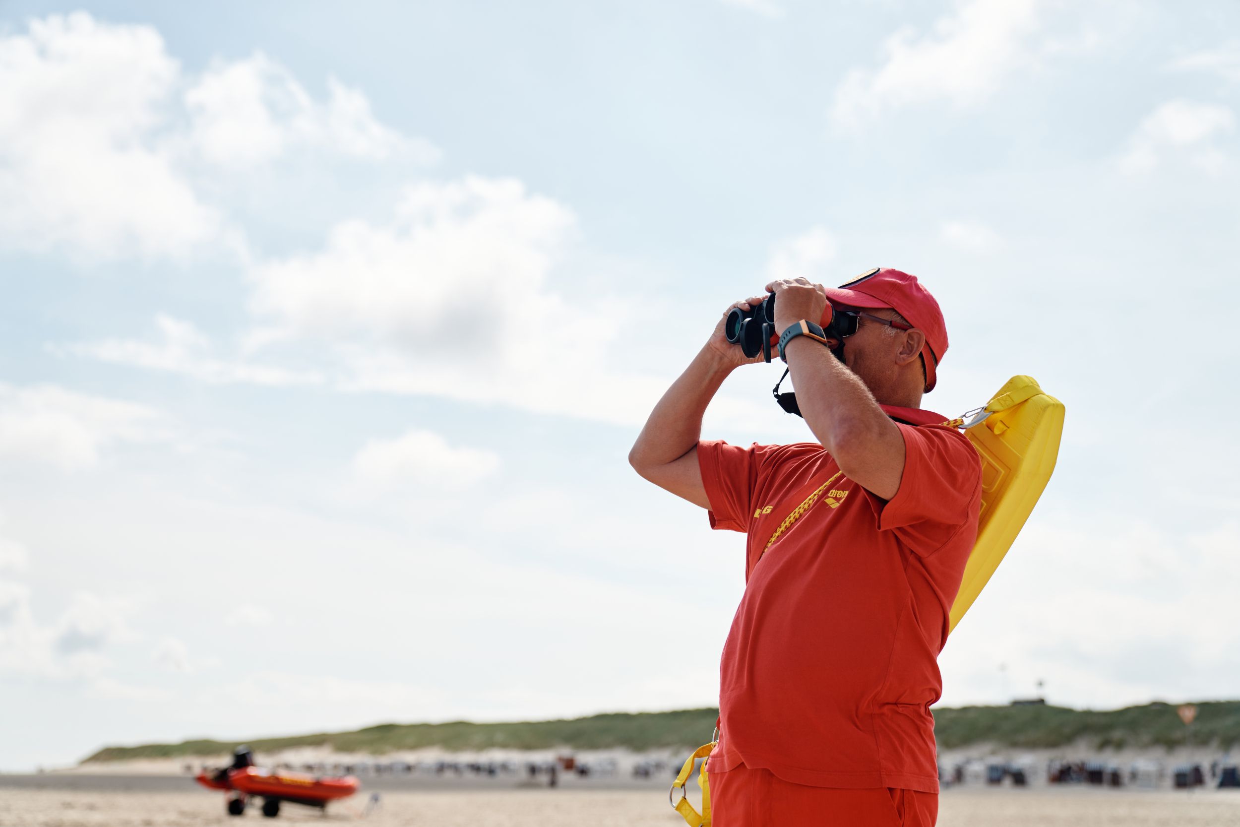 Die Badeaufsicht DLRG blickt am Strand von Spiekeroog durch ein Fernglas.